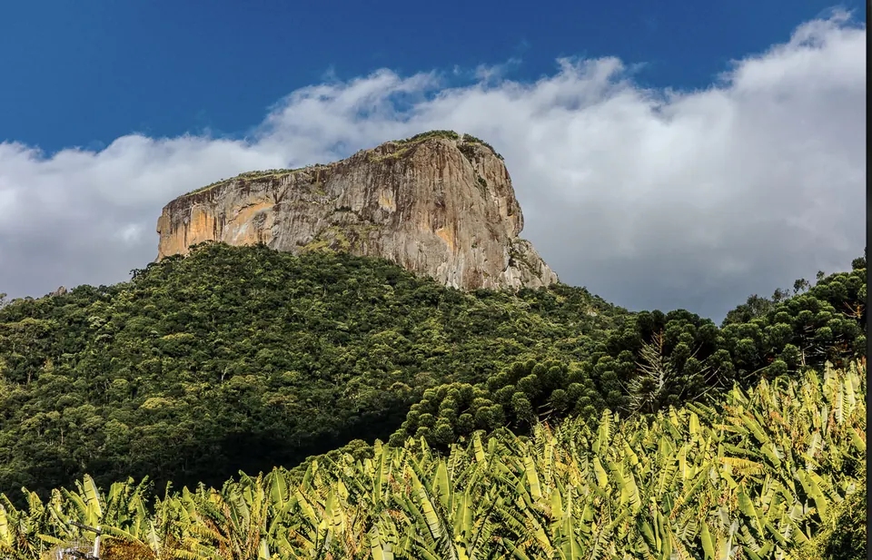 Formação rochosa sobre plantação, sob céu com nuvens